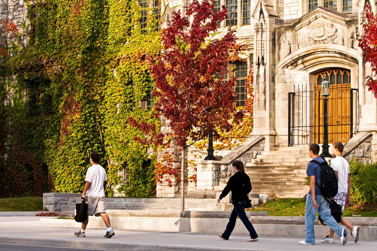 Two people walk past a building on Queen's campus in the fall